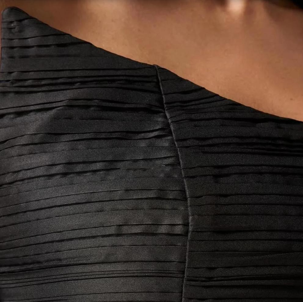 Close-up of the black Candelaria gown featuring elegant horizontal pleated satin fabric and a strapless bodice design.