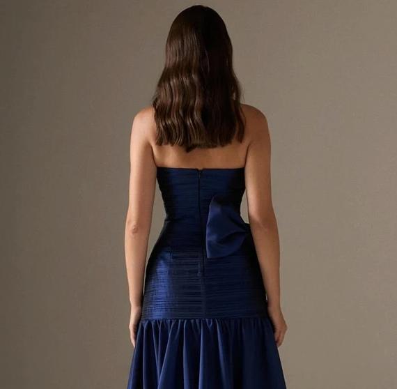 Back view of a navy blue strapless satin A-line gown featuring a pleated bodice and a dramatic bow detail.