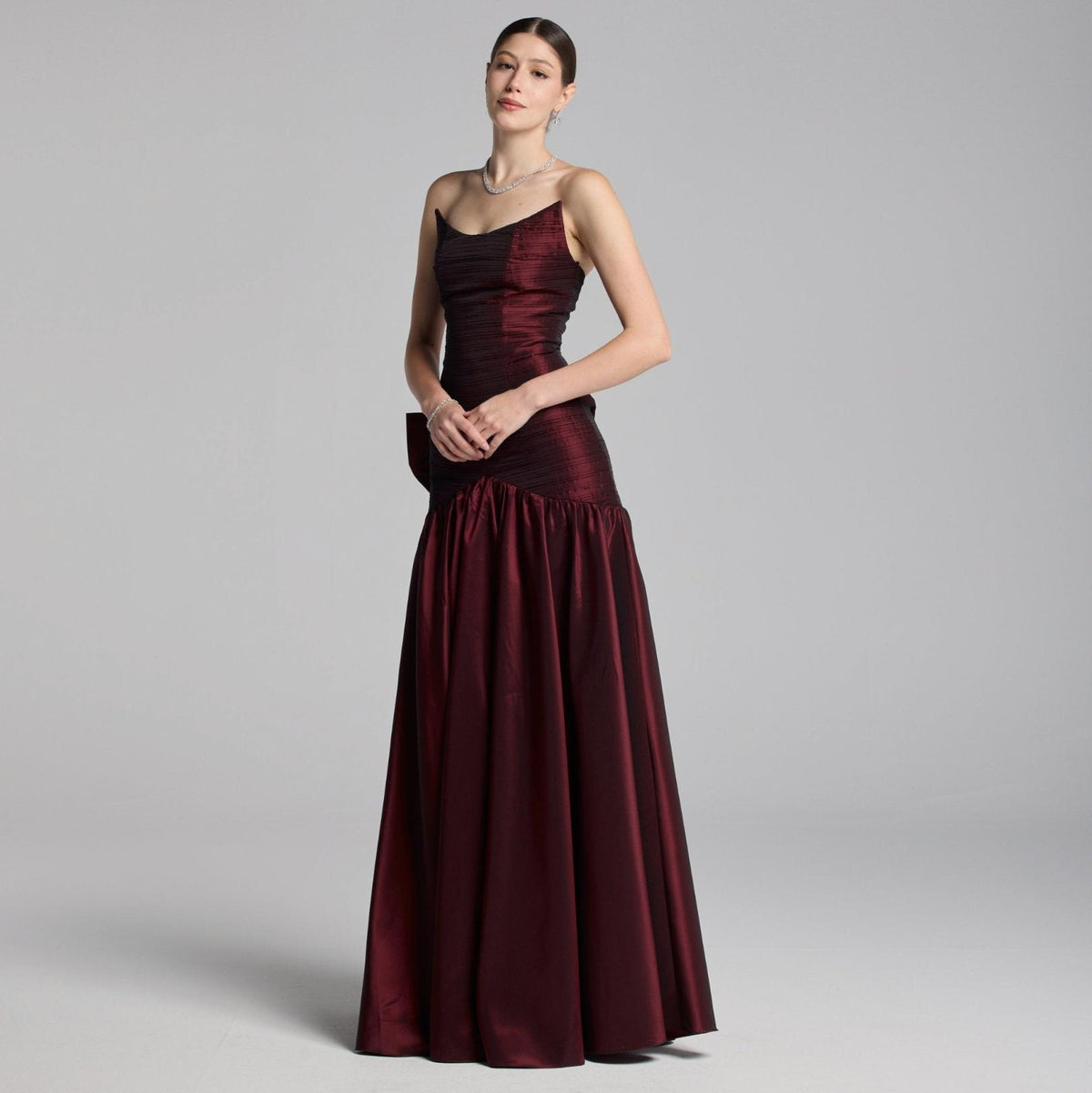 Strapless burgundy satin A-line evening gown with a pleated bodice and dramatic back bow detail.