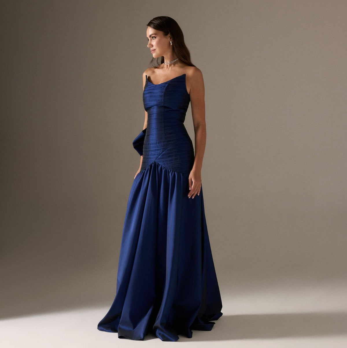 Strapless navy blue satin A-line gown with a pleated bodice and dramatic back bow for formal evening wear.