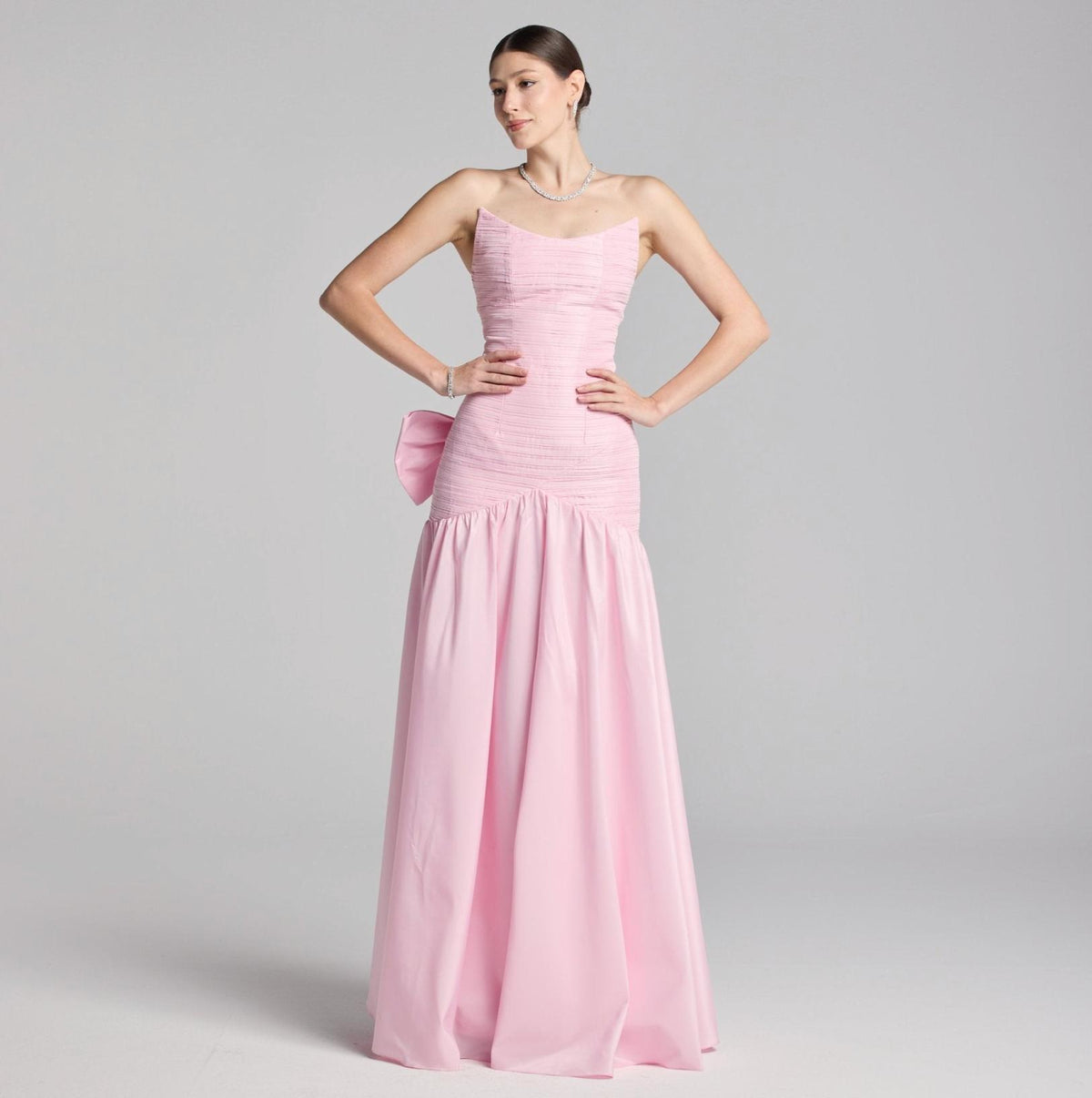 Strapless pink satin A-line evening gown with a pleated bodice and a dramatic bow detail on the back.