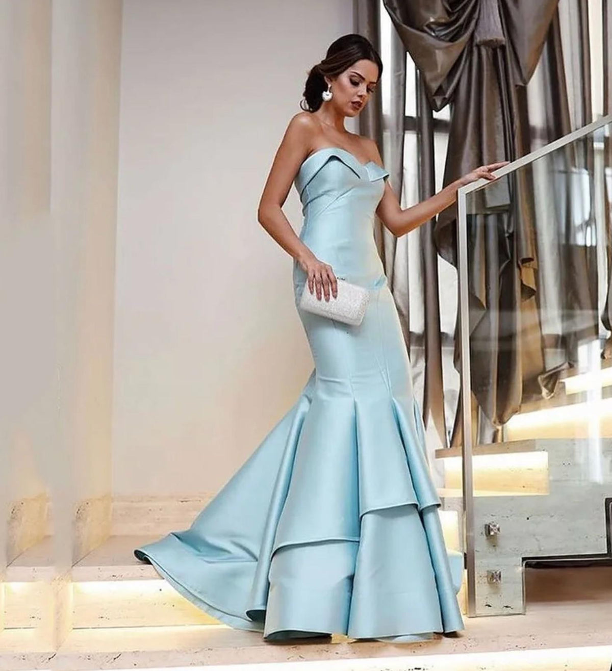 Light blue satin mermaid evening dress with a strapless sweetheart neckline and tiered skirt on a staircase.