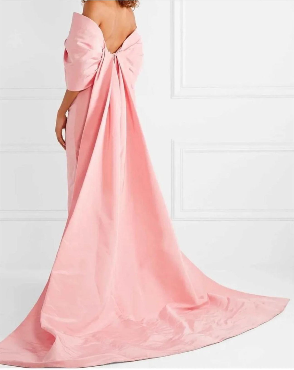 Pink satin off-the-shoulder gown featuring a dramatic back bow and a long, flowing floor-length train.