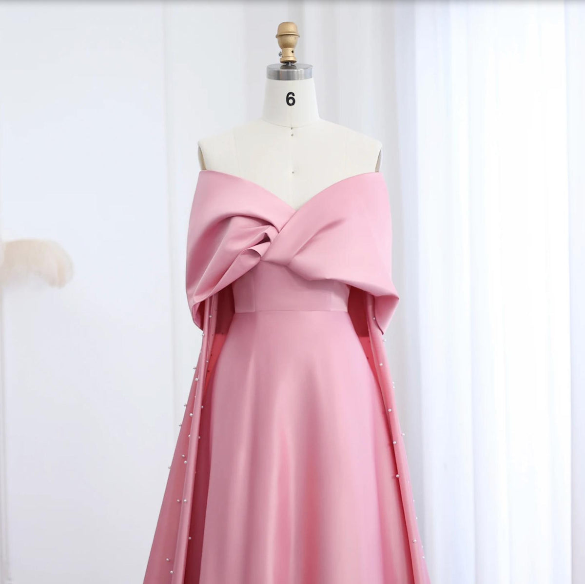 Dubai pink satin off-shoulder gown with cap sleeves, pearl embellishments, and a flowing silhouette on a mannequin.