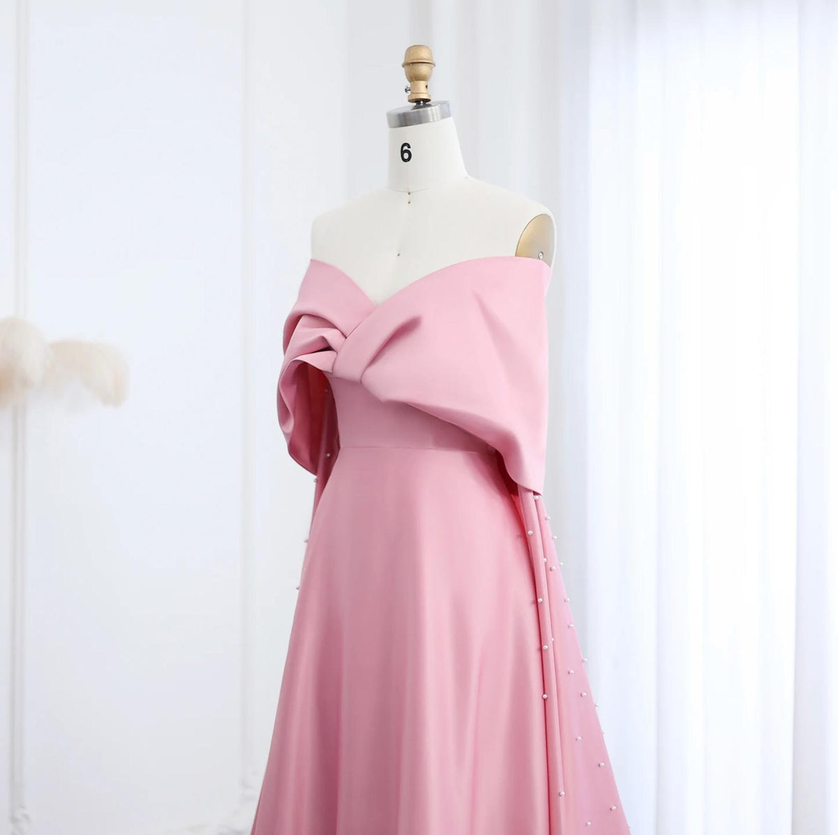Dubai pink satin off-shoulder gown with cap sleeves, pearl embellishments, and a flowing court train on a mannequin.