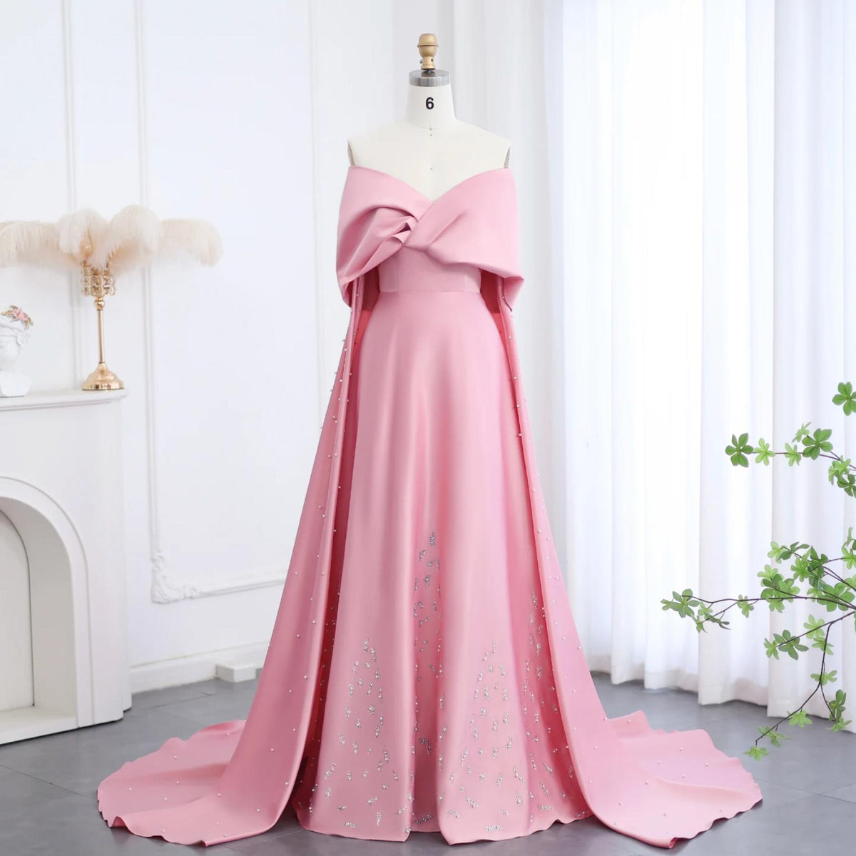 Dubai pink satin off-shoulder gown with cap sleeves, crystal beading, and a dramatic court train on a mannequin.