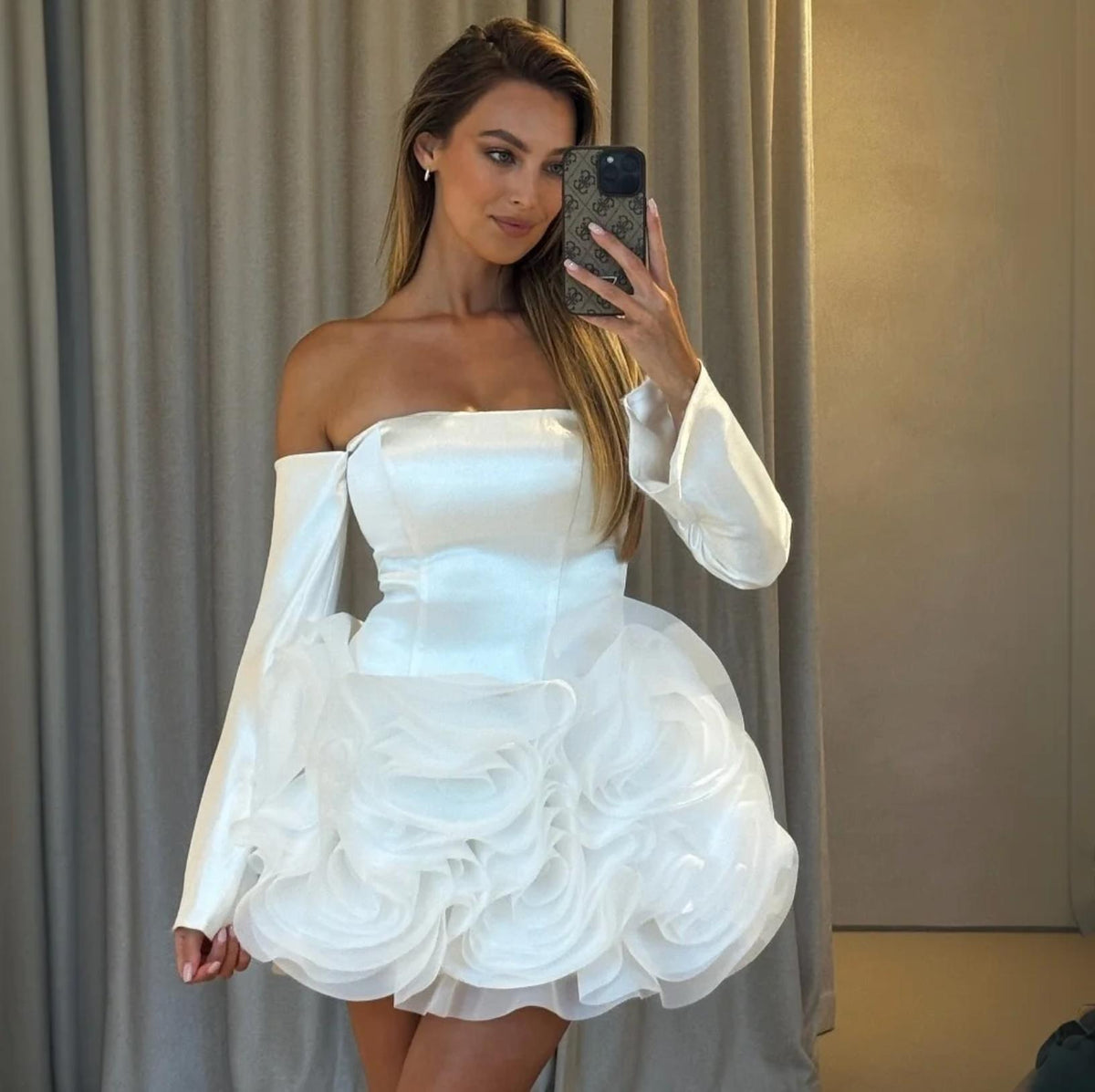 Woman wearing a white strapless satin mini dress with long sleeves and a voluminous organza floral skirt.