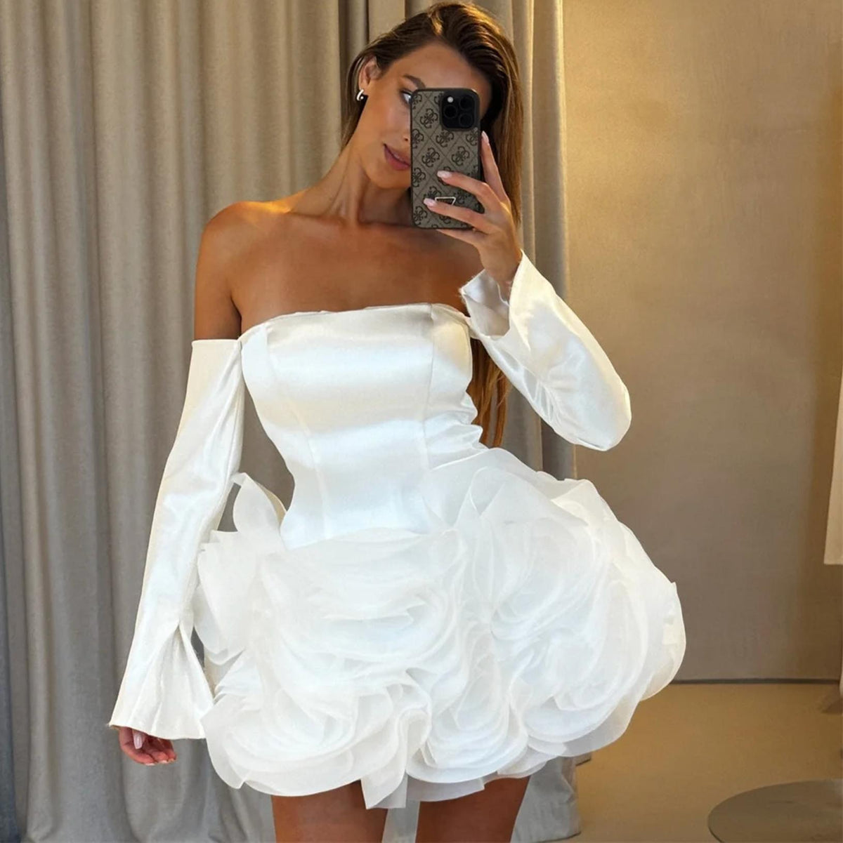 White satin mini dress with strapless bodice, long sleeves, and voluminous organza floral skirt details.