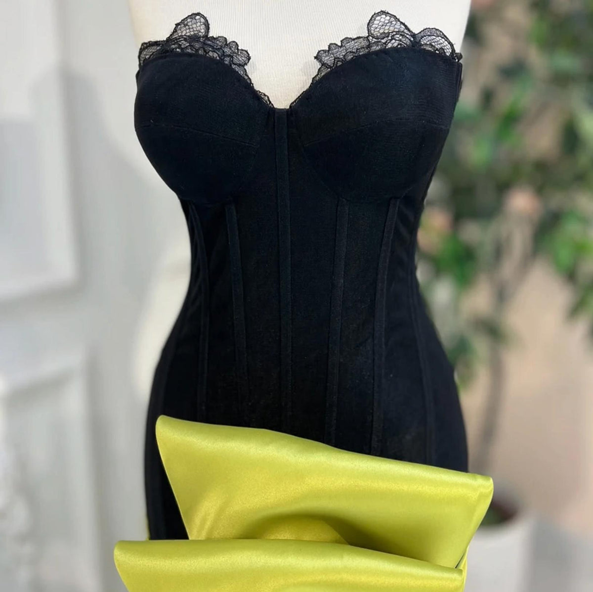 Black corset mermaid gown with a sweetheart neckline, lace trim, and a vibrant lime green satin bow accent.