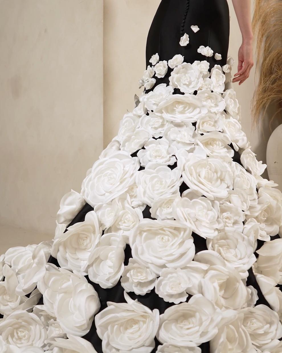 Black satin mermaid gown featuring a dramatic train adorned with large, layered white floral appliqués.