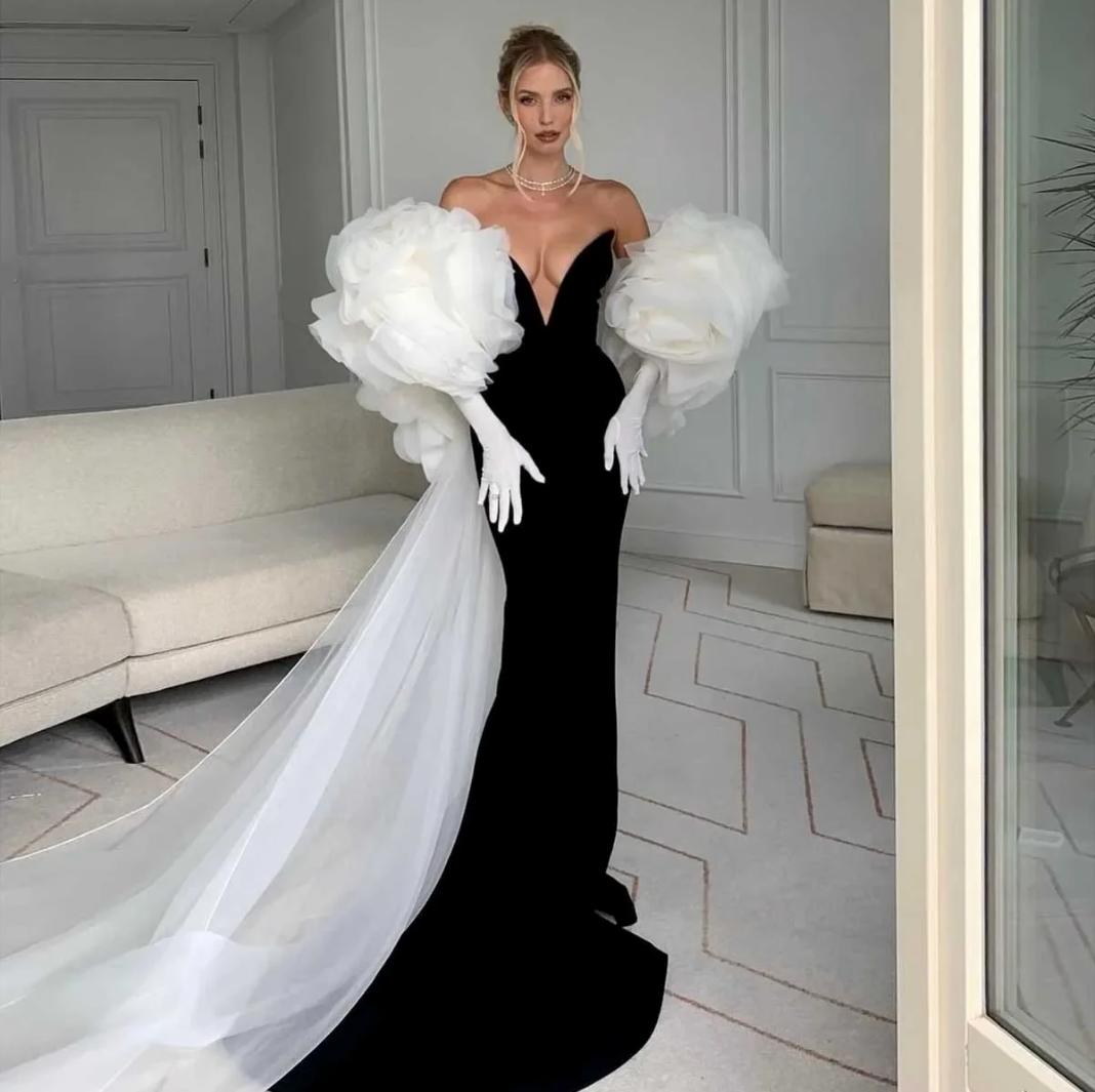 Black mermaid-cut satin gown with a deep neckline, dramatic white tulle ruffled sleeves, and a flowing floor-length train.