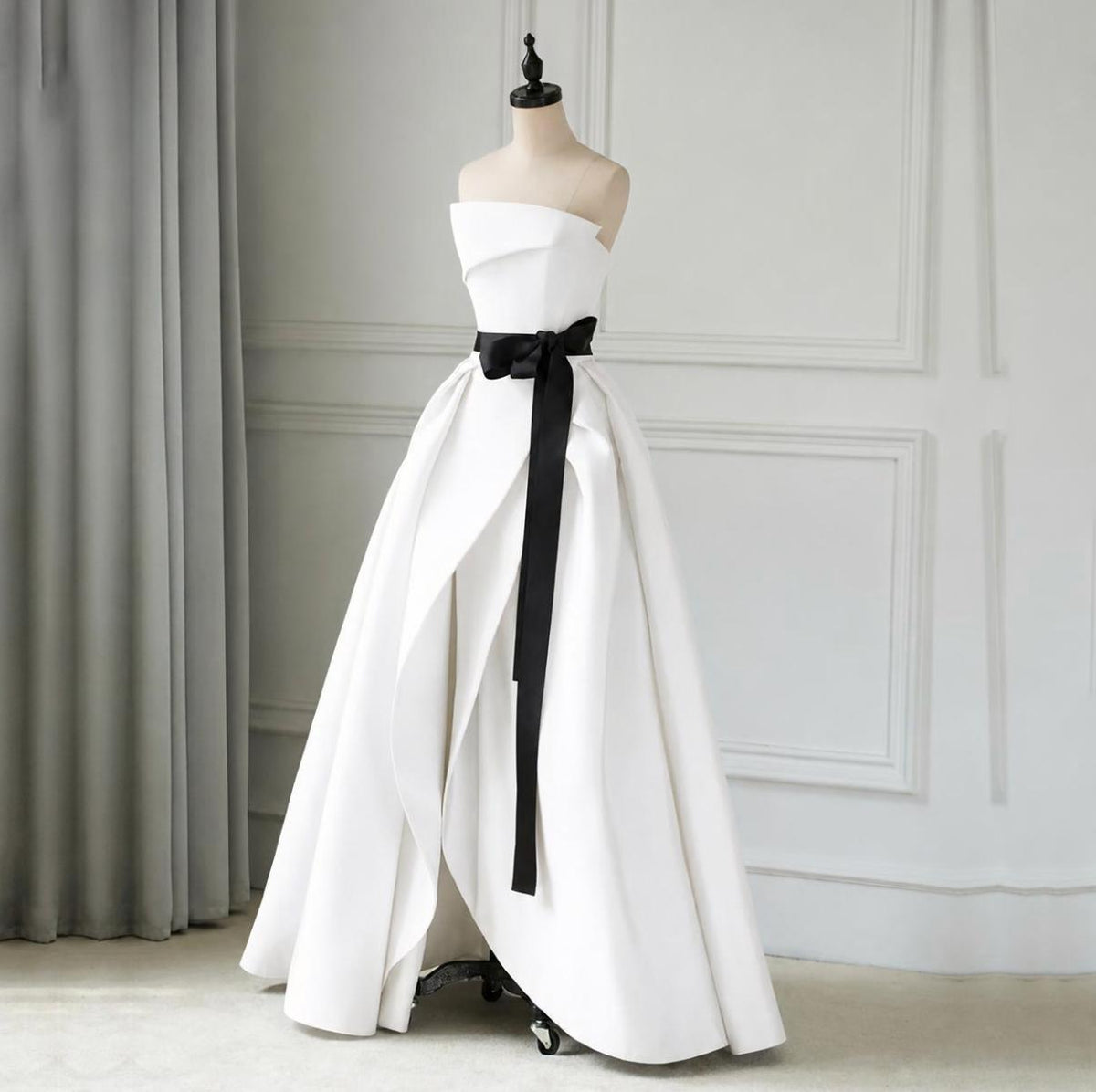 Strapless white satin twill A-line gown with a black sash and pleated floor-length skirt on a mannequin.