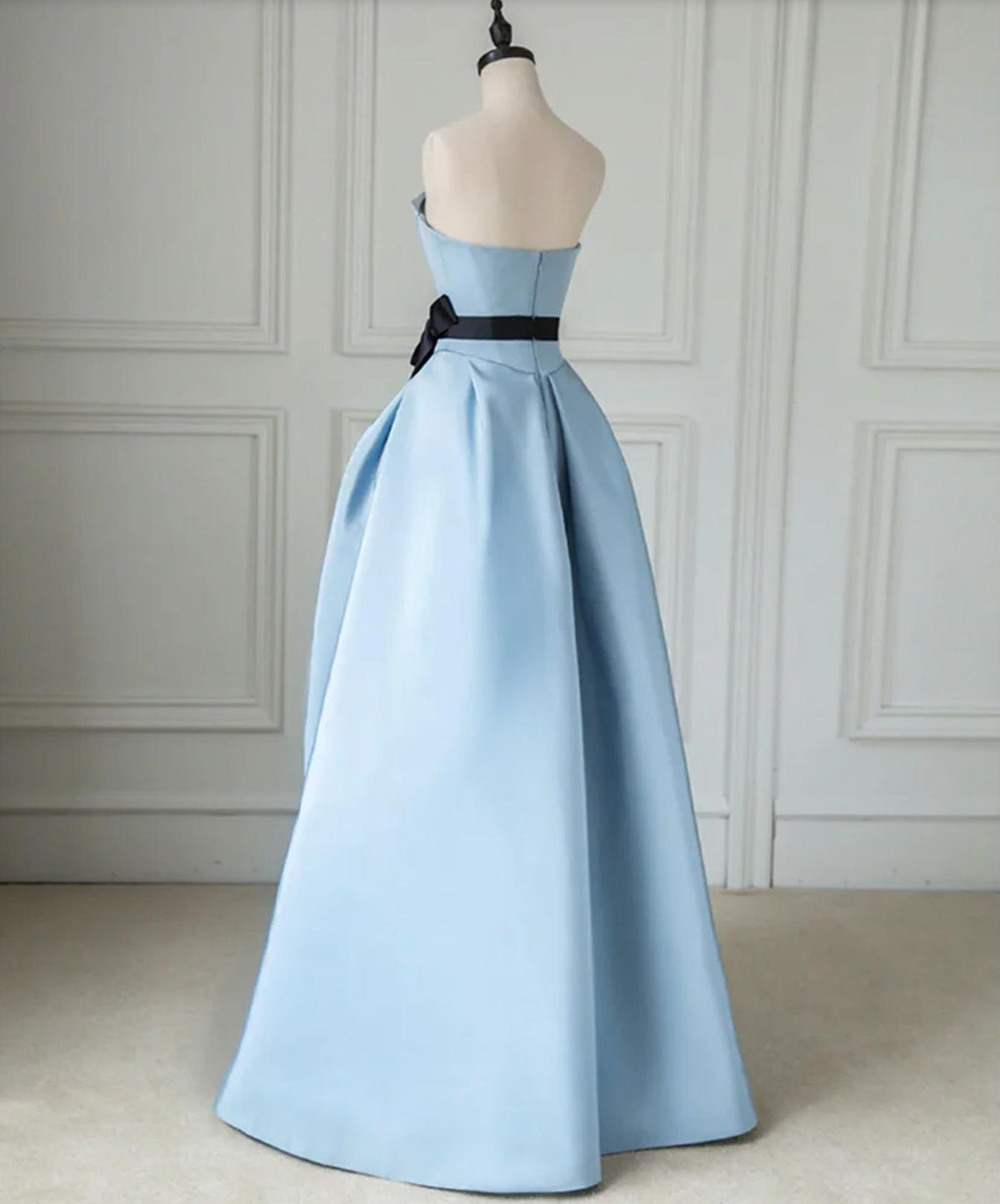 Strapless light blue satin twill A-line gown with a black waist sash and pleated floor-length skirt on a mannequin.