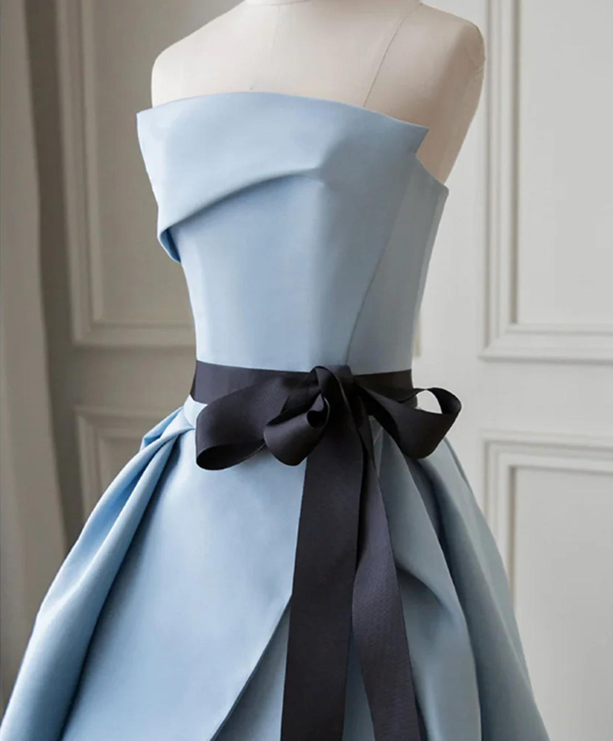 Strapless light blue satin twill Crete gown with a pleated bodice and a contrasting black sash tied at the waist.