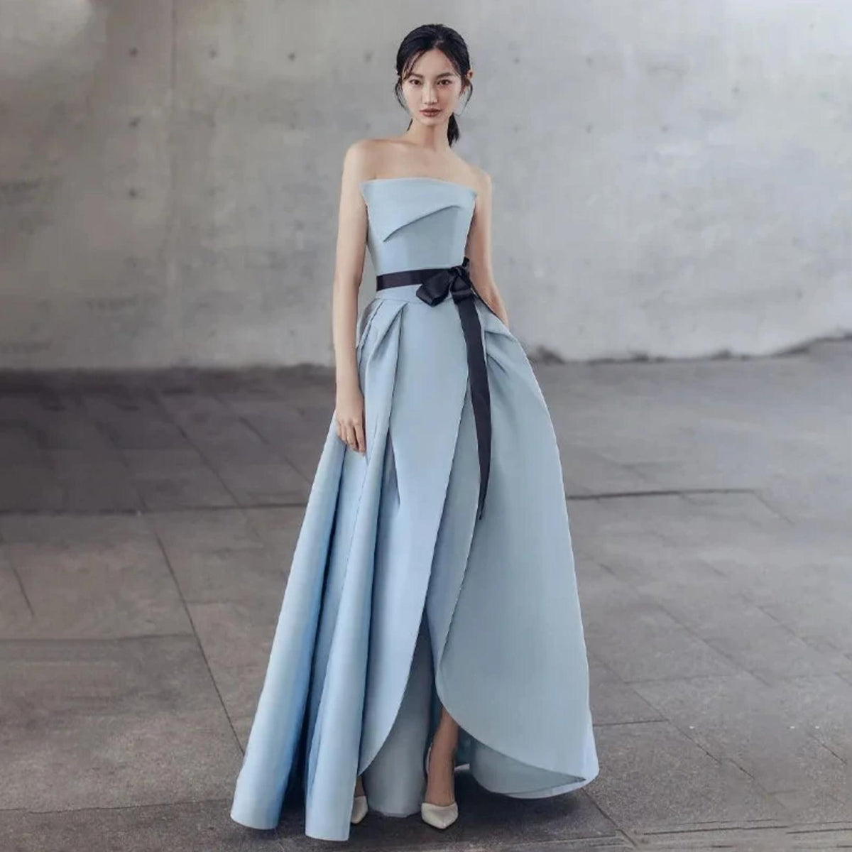 Strapless light blue Crete gown with a pleated A-line skirt, side ruching, and a contrasting black waist sash.