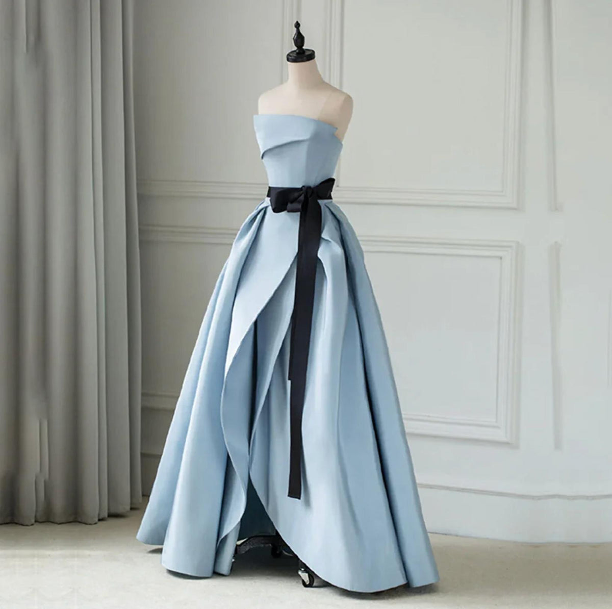 Strapless light blue satin twill A-line gown with a black sash, pleated ruching, and a dramatic floor-length skirt.