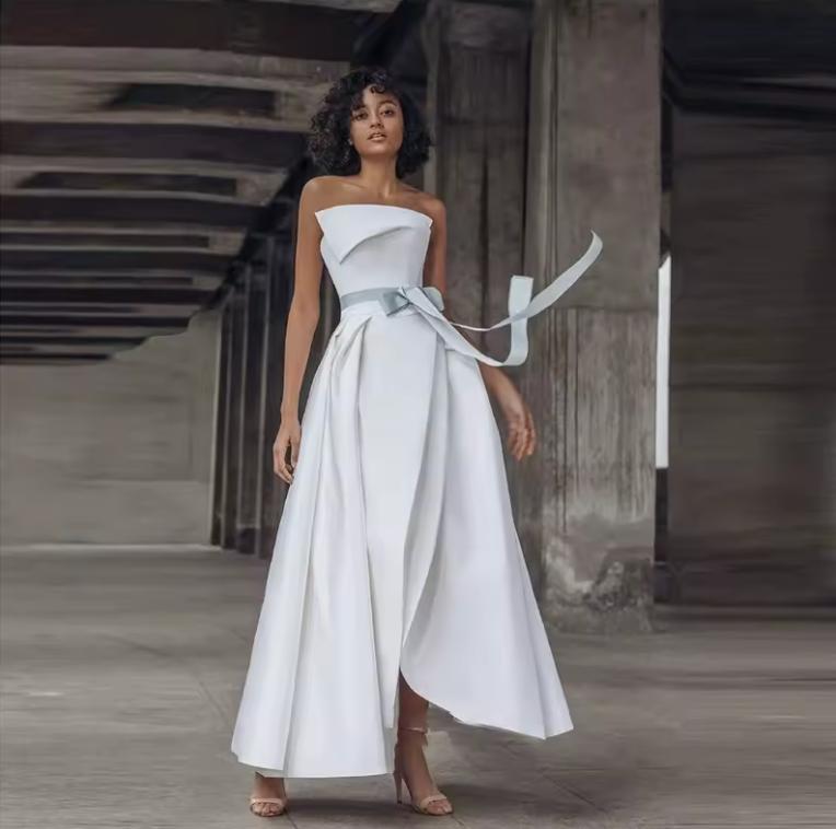 Strapless white satin twill Crete gown with a pleated A-line skirt, cinched waist sash, and elegant floor-length silhouette.