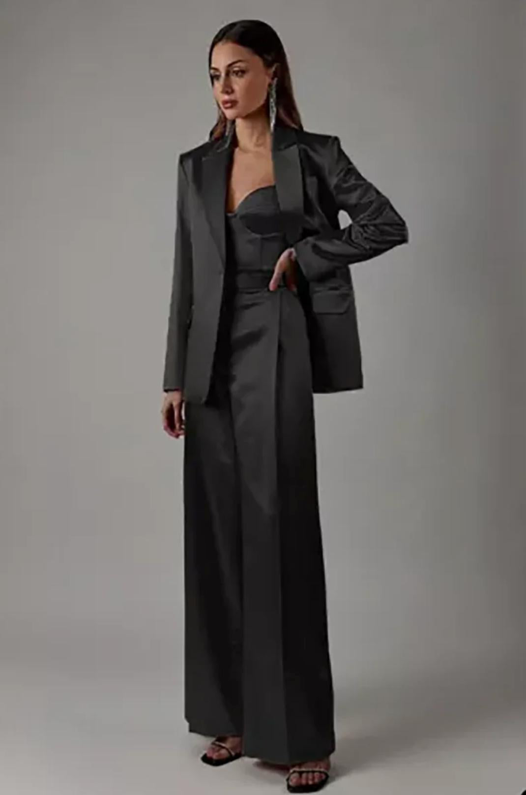 Model wearing a sleek black satin two-piece suit with a single-button blazer and high-waisted wide-leg trousers.