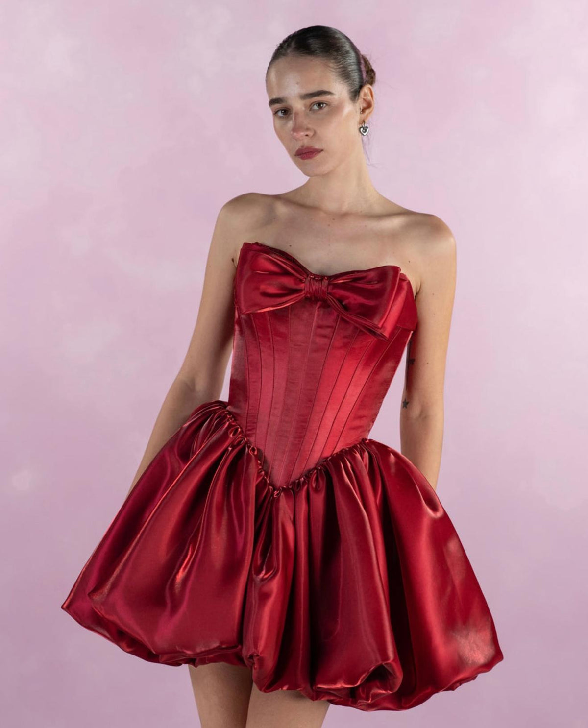 Strapless red satin mini dress with a pleated bodice, large front bow, and voluminous A-line skirt.