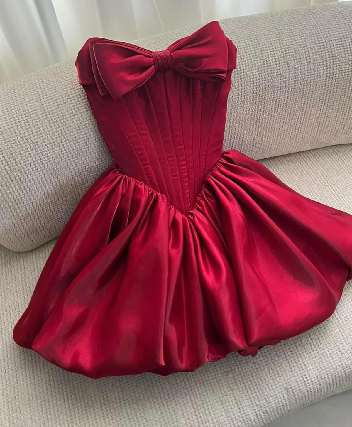 Strapless red satin mini dress with a structured bodice, large bow detail, and a voluminous pleated A-line skirt.