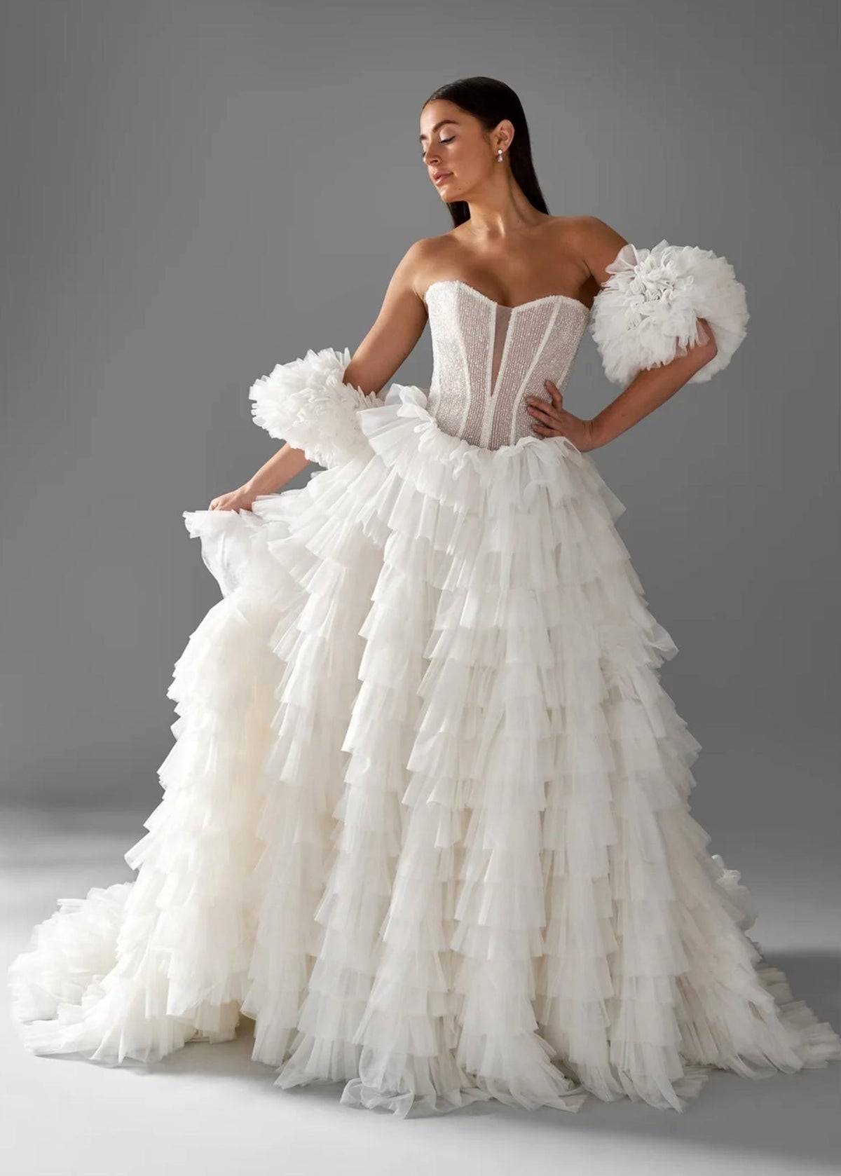 White strapless A-line ball gown with a beaded corset bodice, tiered chiffon ruffles, and dramatic ruffled sleeves.
