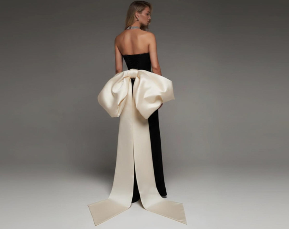 Strapless black mermaid wedding dress with a dramatic oversized white satin bow and long train.