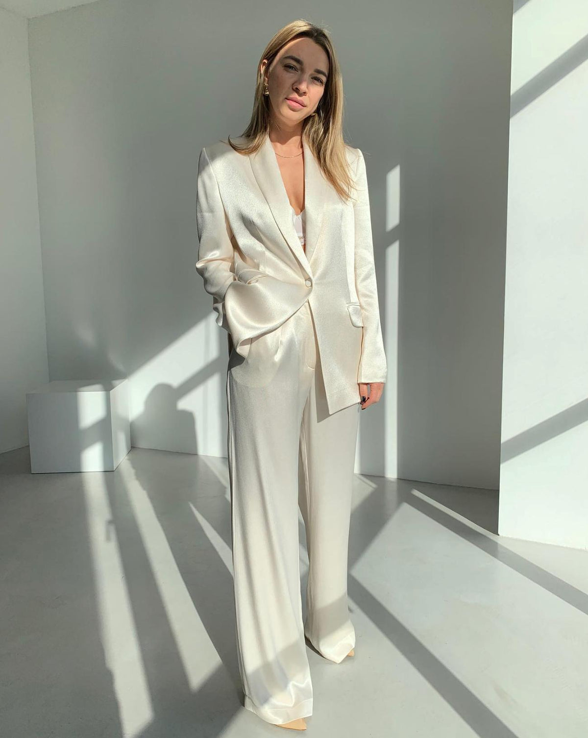 Woman wearing a cream satin two-piece suit with a single-button shawl lapel jacket and wide-leg trousers.
