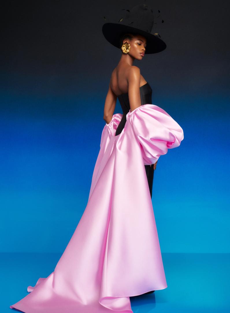 Strapless black satin evening gown with a dramatic, detachable pink puff sleeve cape and a wide-brimmed black hat.