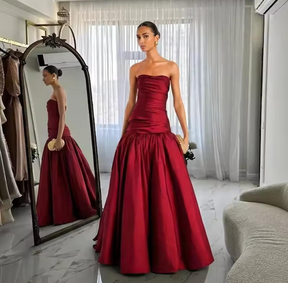 Strapless burgundy taffeta gown with a hand-draped bodice and a voluminous, structured floor-length skirt.