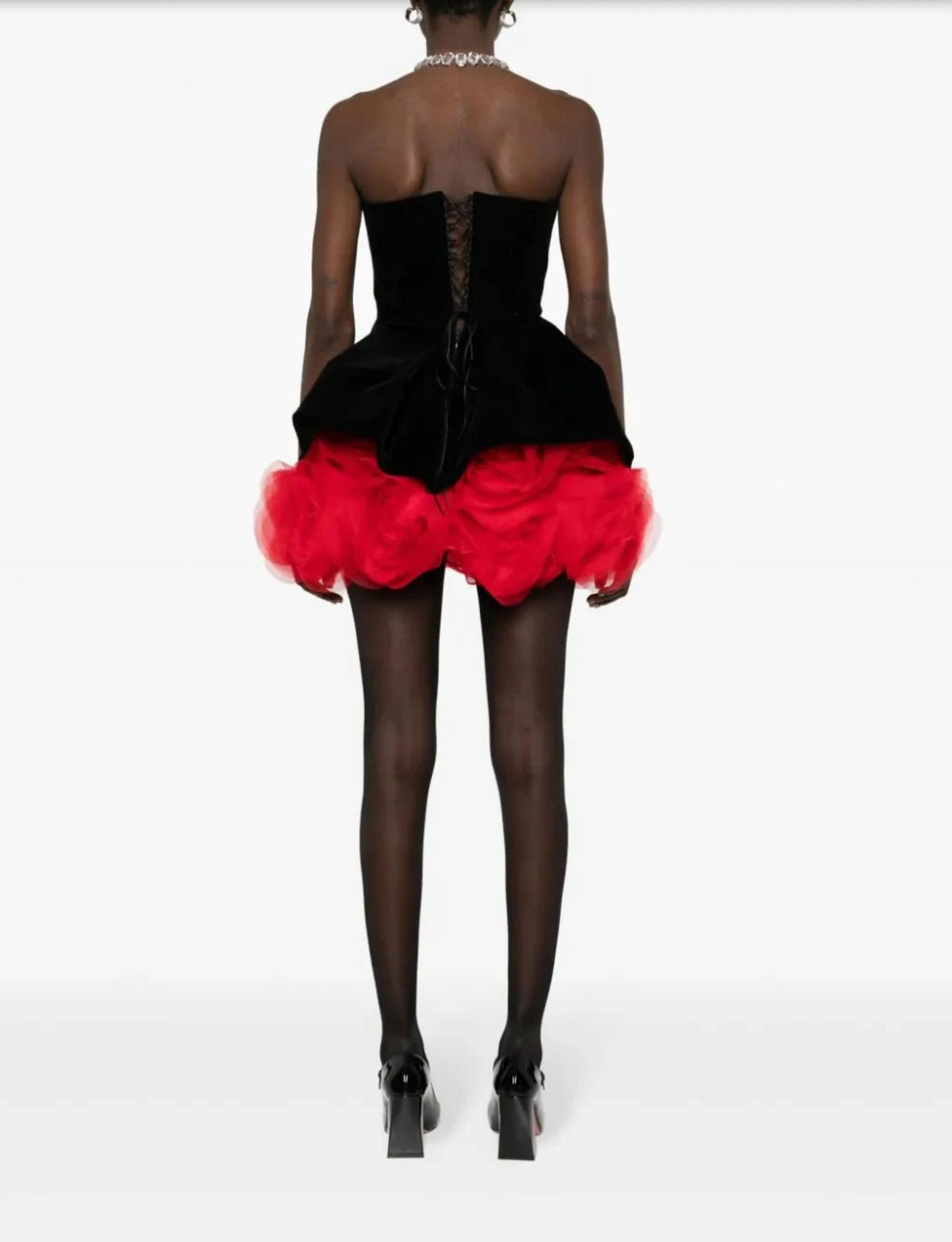 Back view of a strapless black velvet mini dress with a voluminous red tulle skirt and lace-up corset detail.