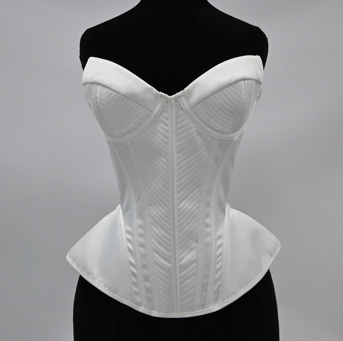 White structured corset bustier with sweetheart neckline, intricate chevron stitching, and a flared peplum waist.