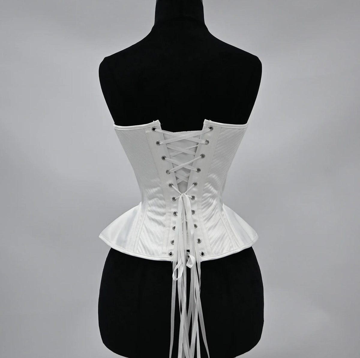 White structured corset bustier with a lace-up back closure and elegant quilted detailing on a black mannequin.