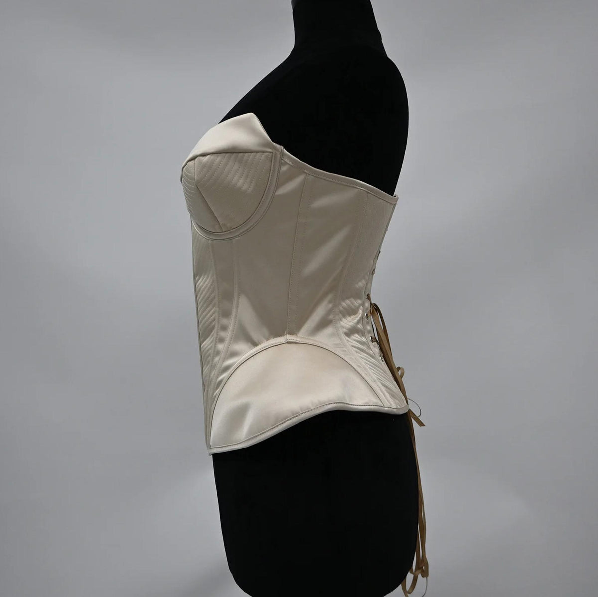 Cream-colored structured corset bustier with quilted detailing and a lace-up back on a mannequin.