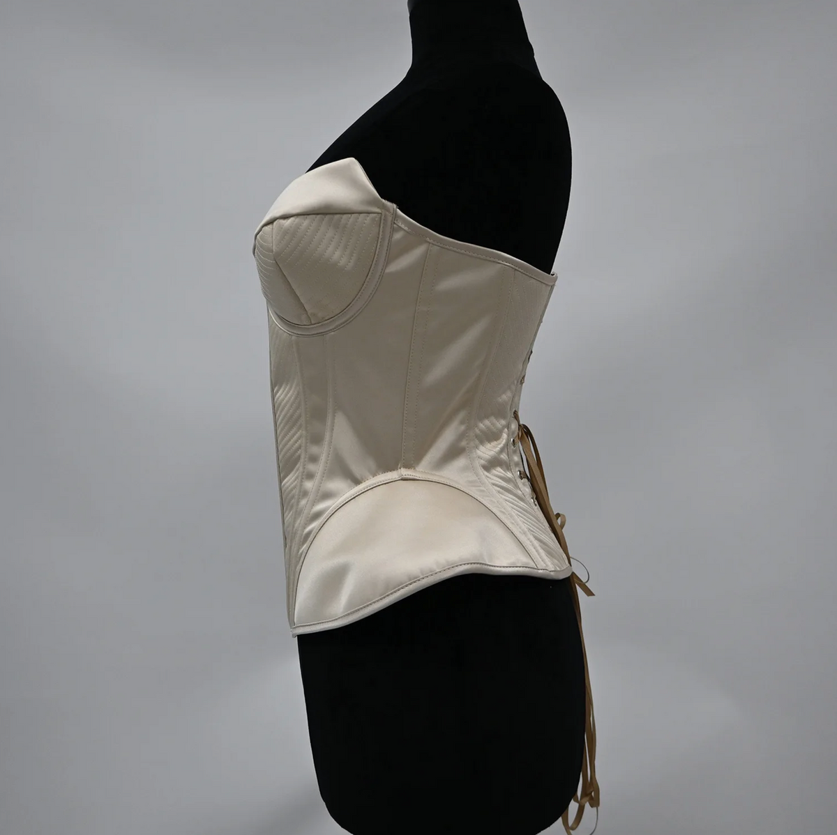Cream-colored structured corset bustier with quilted detailing and a lace-up back on a mannequin.