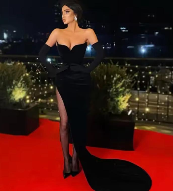 Strapless black velvet evening gown with a sweetheart neckline, side slit, and matching opera gloves on a red carpet.