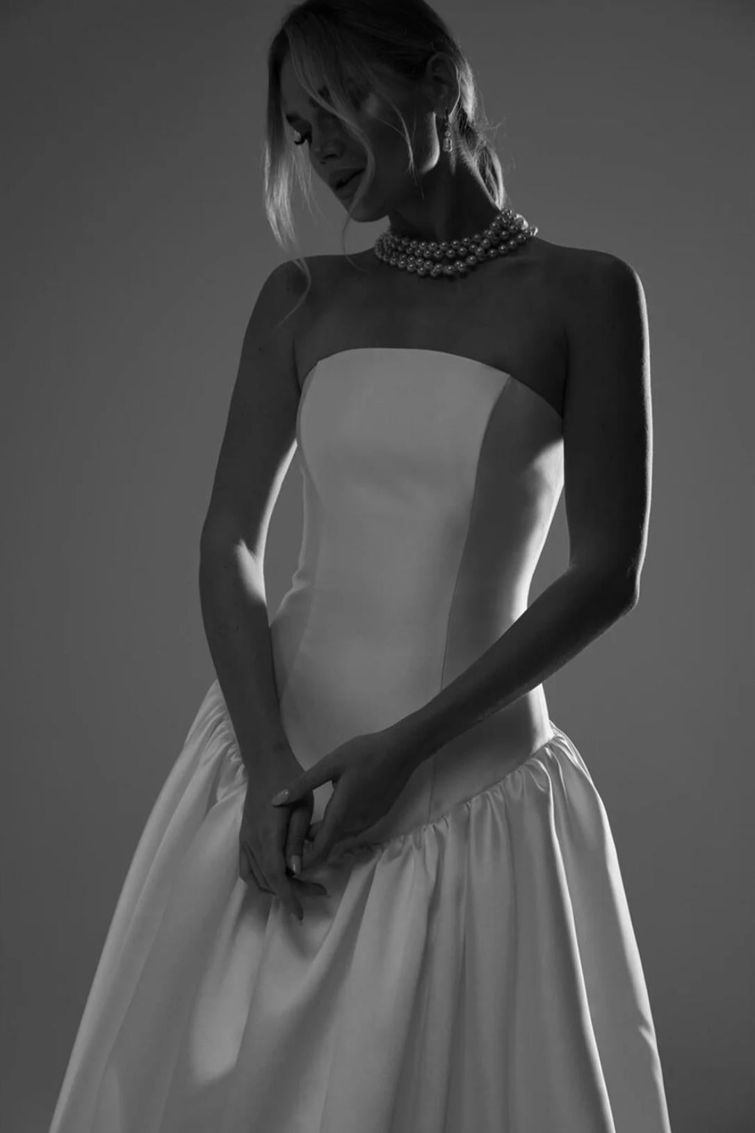 Woman wearing a strapless white satin A-line Espanola gown with a natural waistline and a multi-strand pearl necklace.