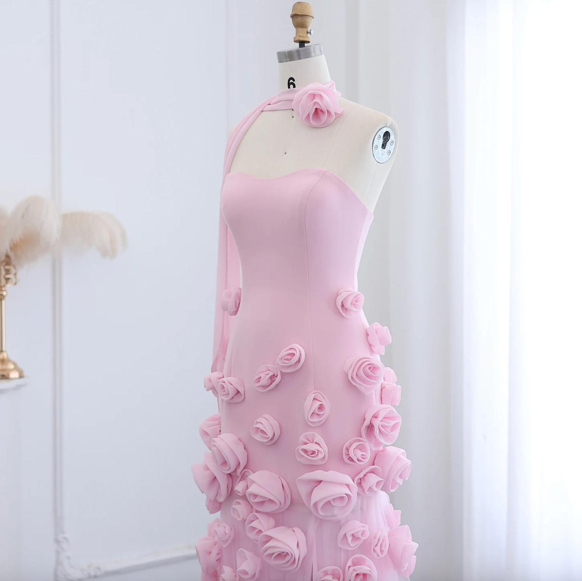 Pink trumpet gown with sweetheart neckline, 3D floral appliqués, and tulle detailing on a dress form.