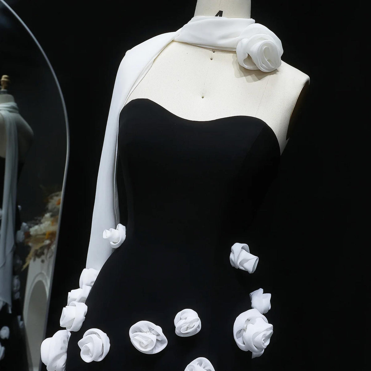 Black sweetheart gown with white 3D floral appliqués and a draped white shoulder scarf on a mannequin.