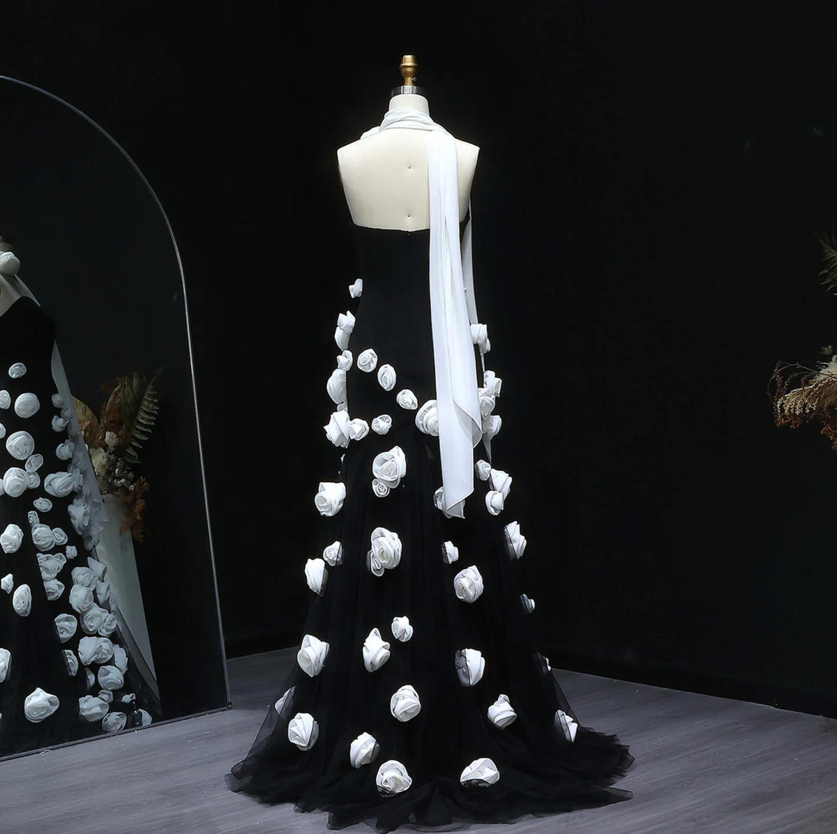 Black trumpet gown with white 3D floral appliqués, sweetheart neckline, and a flowing tulle train on a mannequin.