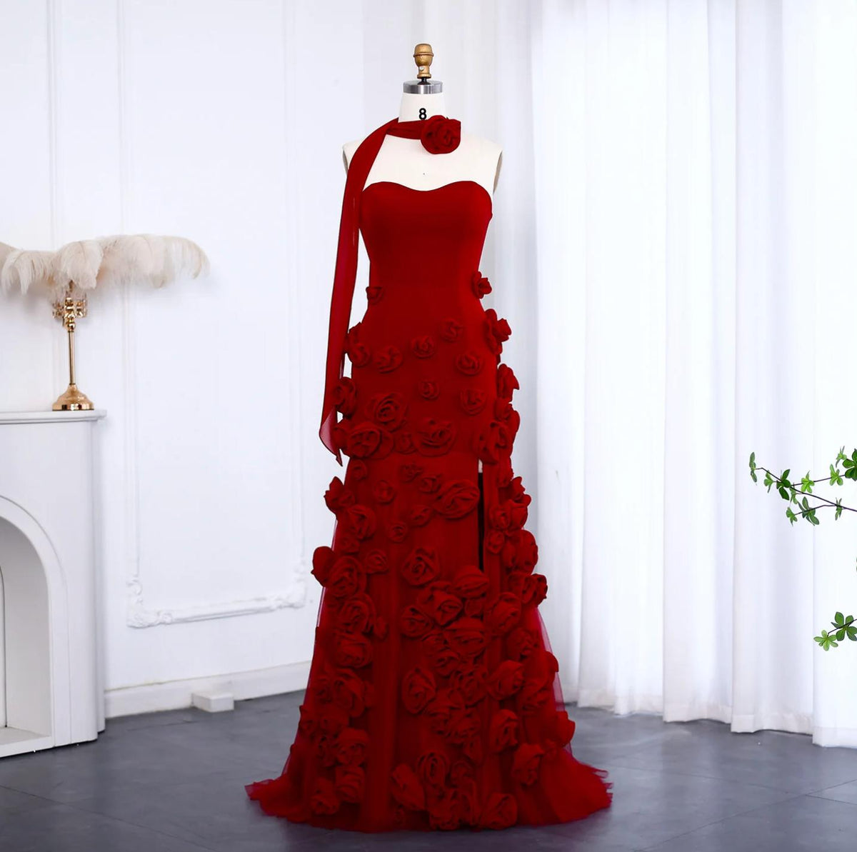 Red trumpet gown with sweetheart neckline, 3D floral appliqués, side slit, and matching neck scarf on a mannequin.