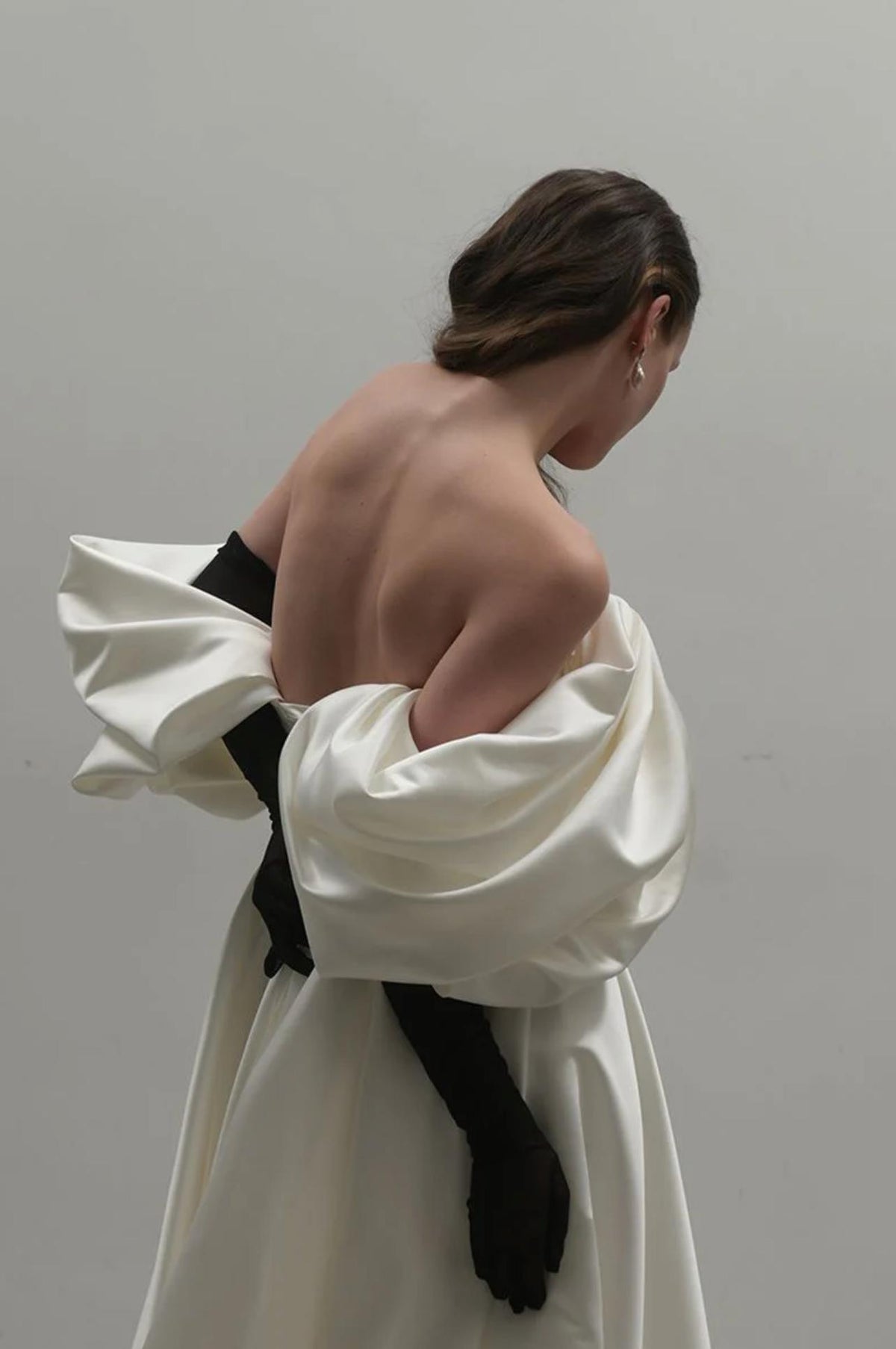 Off-shoulder white satin A-line gown with dramatic pleated sleeves and long black gloves.