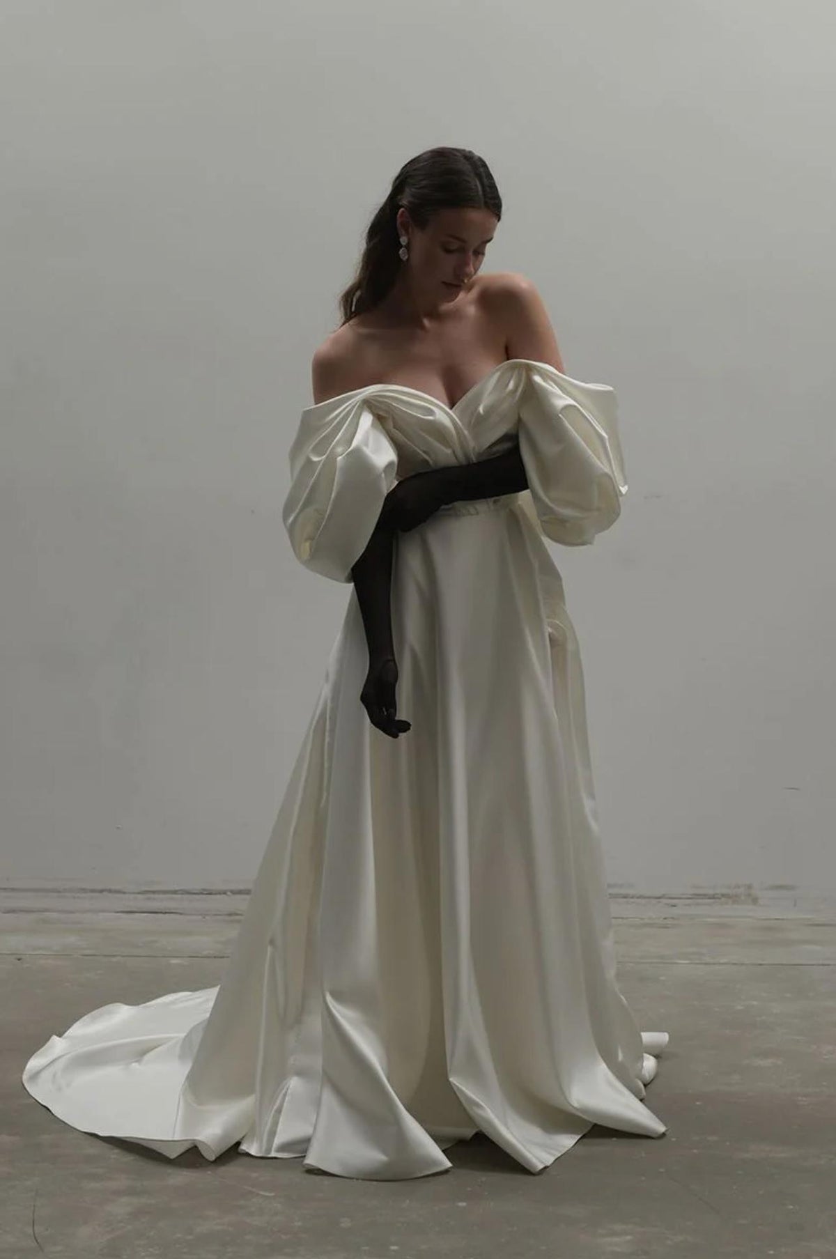 Elegant white satin A-line gown with off-shoulder puff sleeves and a floor-length skirt, styled with black gloves.