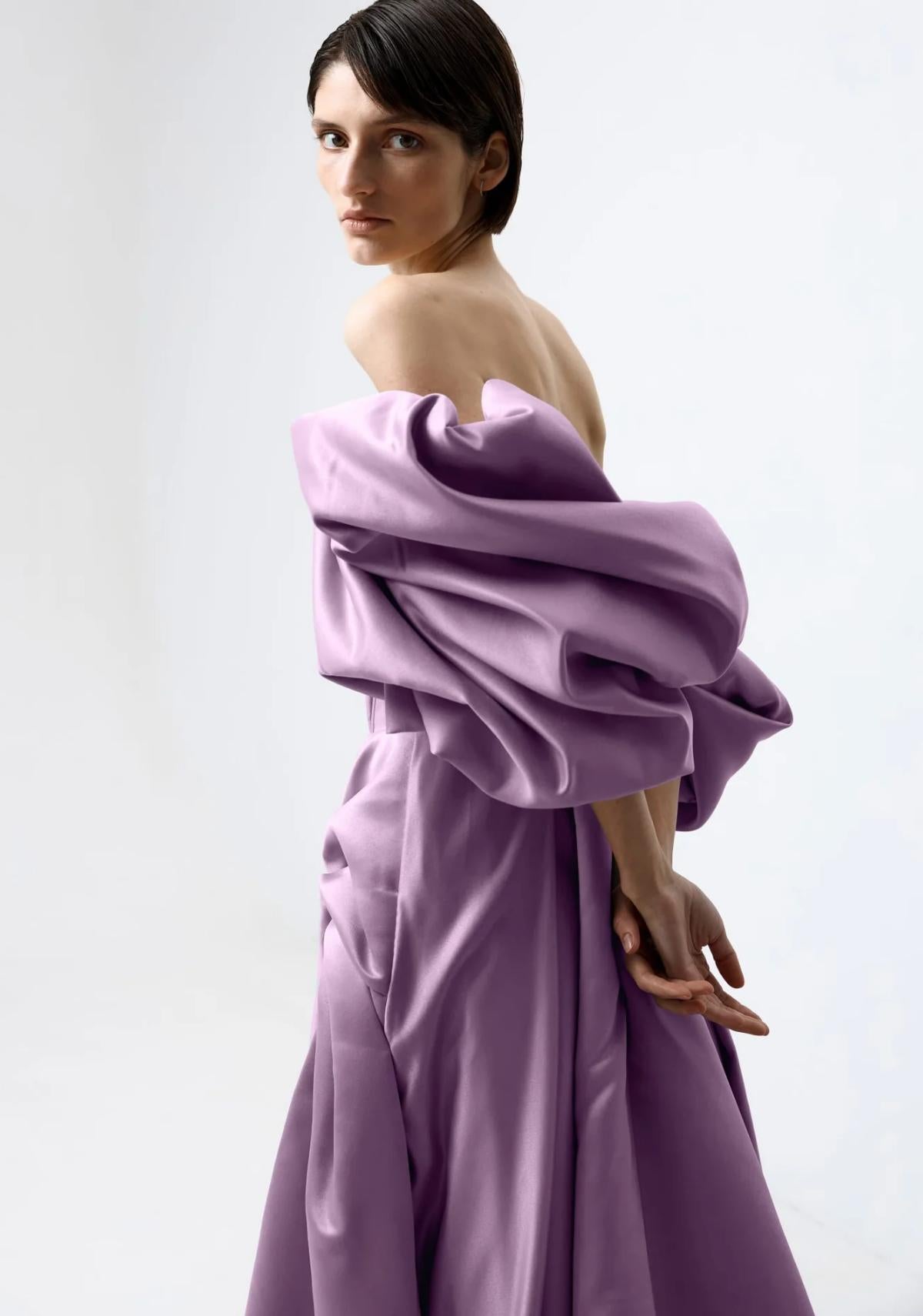 Model wearing a lavender off-shoulder satin A-line gown with voluminous pleated sleeves and a formal vintage design.