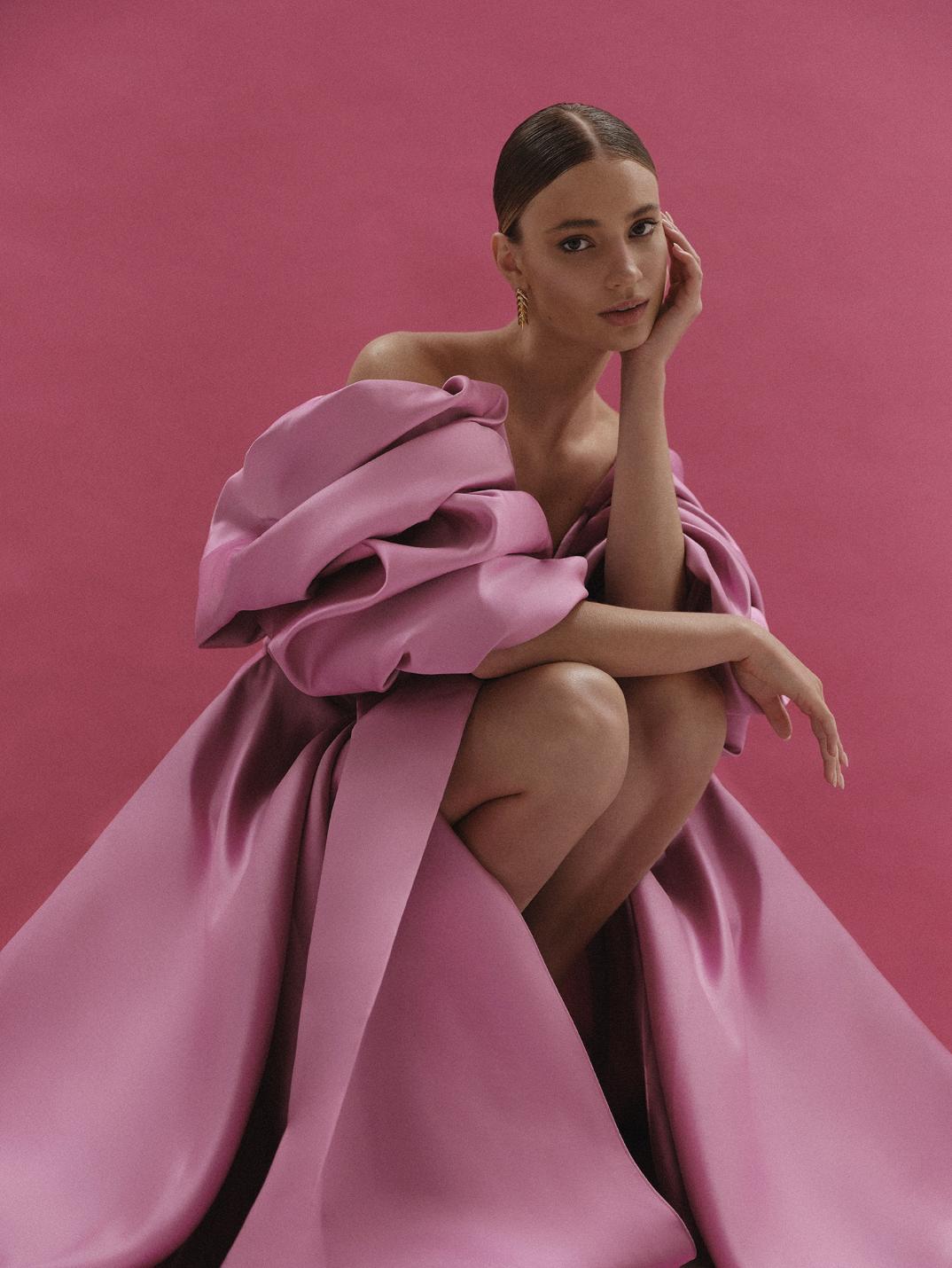 Model wearing a pink off-shoulder satin A-line gown with voluminous pleated sleeves and a high side slit.
