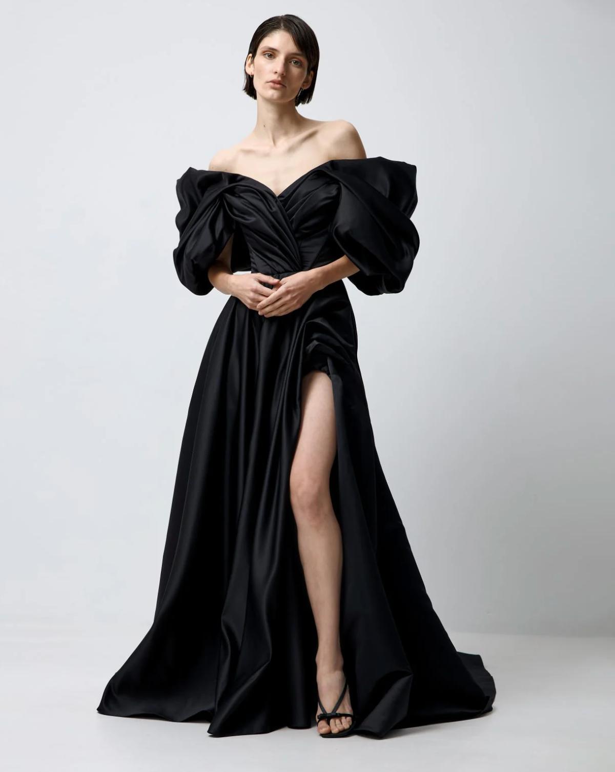 Black satin A-line gown with off-shoulder puff sleeves, pleated bodice, and a high side slit on a model.