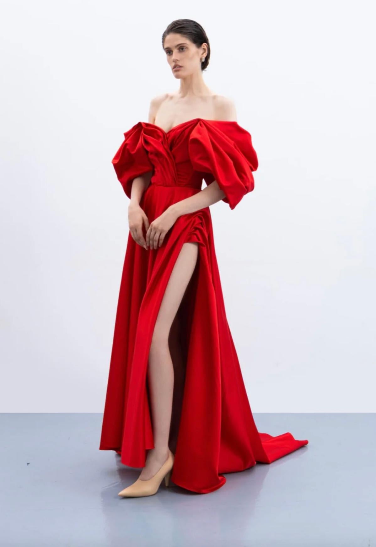 Red off-shoulder satin A-line gown with voluminous sleeves, pleated bodice, and a high side slit.