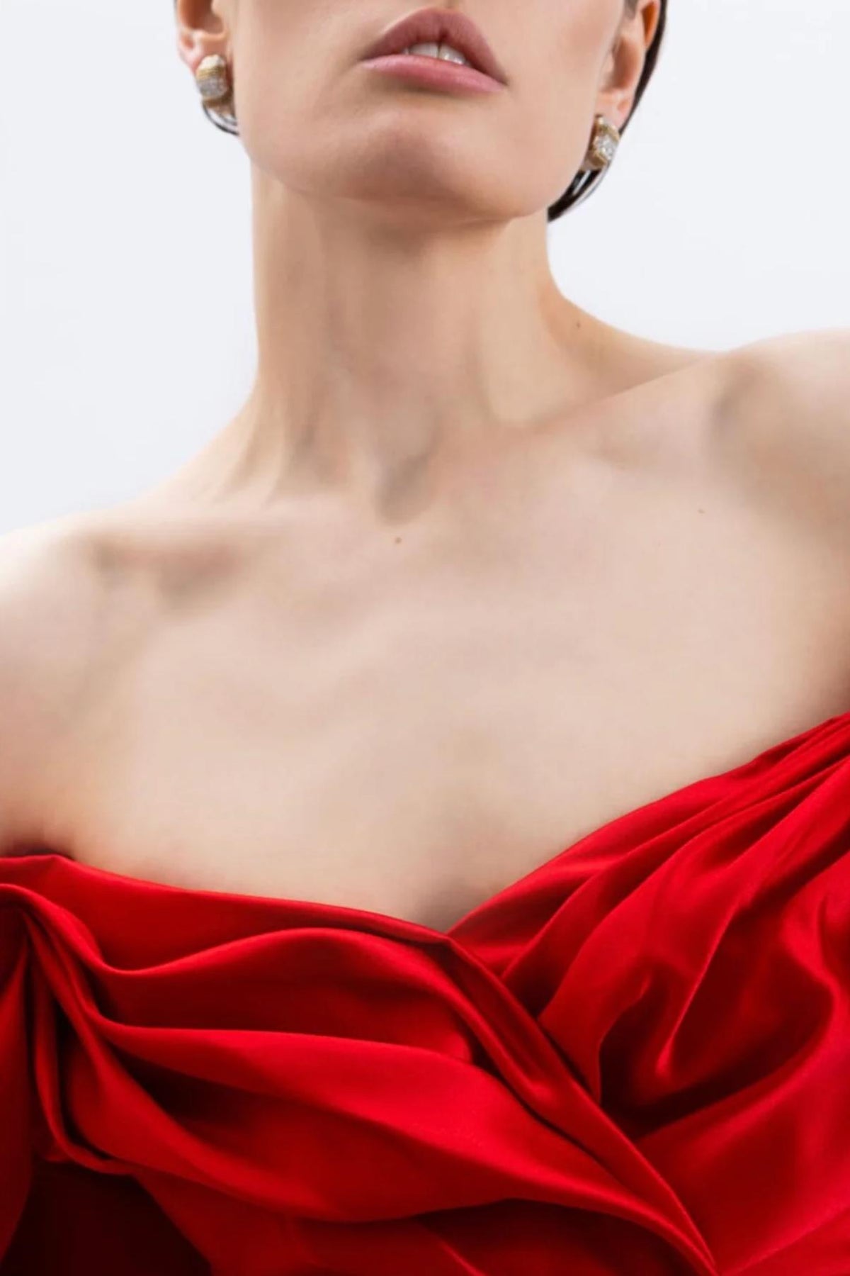 Close-up of a model wearing a luxurious red satin off-shoulder gown with elegant pleated detailing.