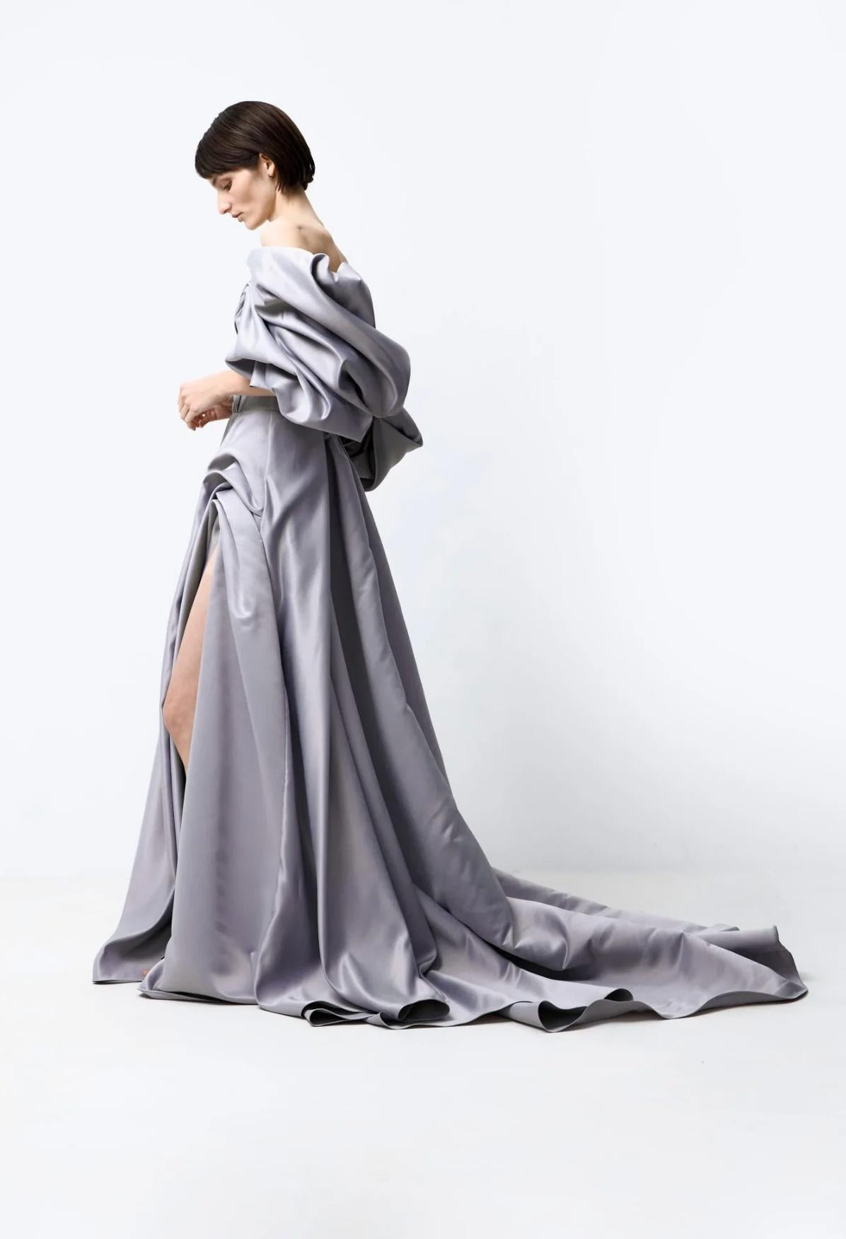 Grey off-shoulder satin A-line gown with voluminous pleated sleeves, a high side slit, and a dramatic floor-length train.