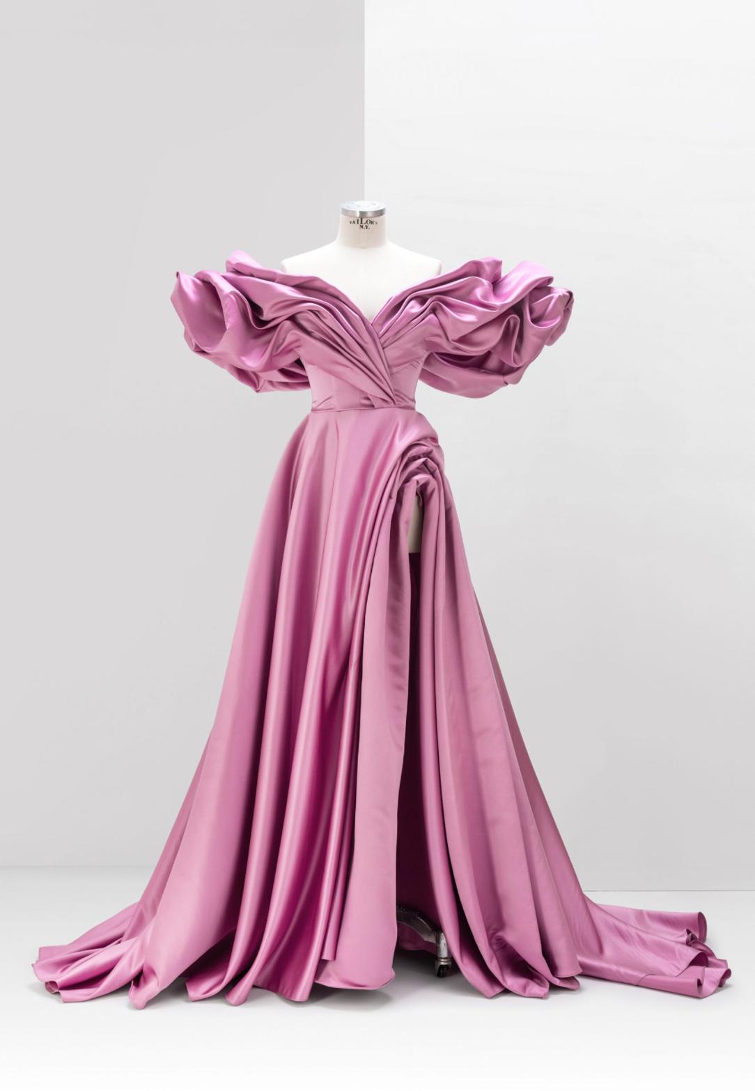 Pink satin A-line gown with off-shoulder pleated sleeves, a high side slit, and a floor-length skirt on a mannequin.