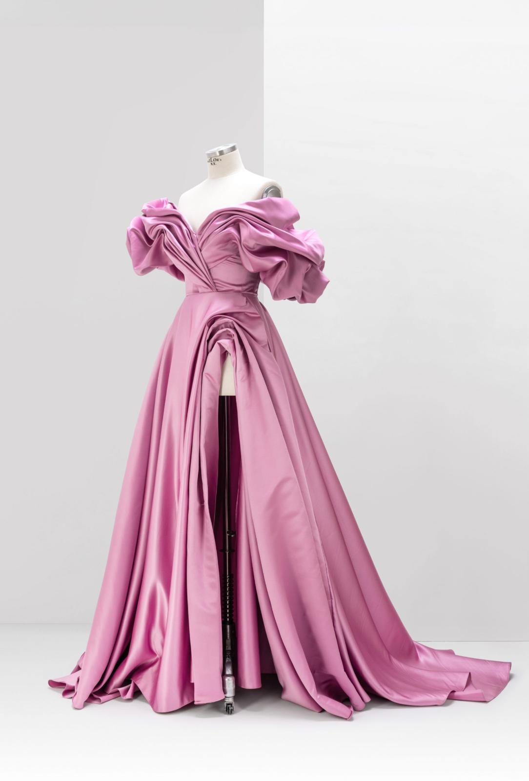 Pink off-shoulder satin A-line gown with voluminous pleated sleeves and a high side slit on a dress form.